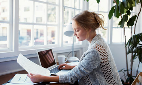 Woman reading paper and laptop