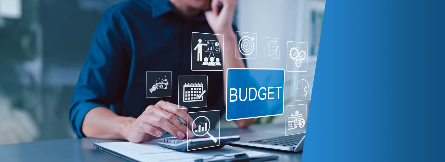 A person sitting behind a laptop with a pen in their hand resting over a calculator, with text popped up saying budget.