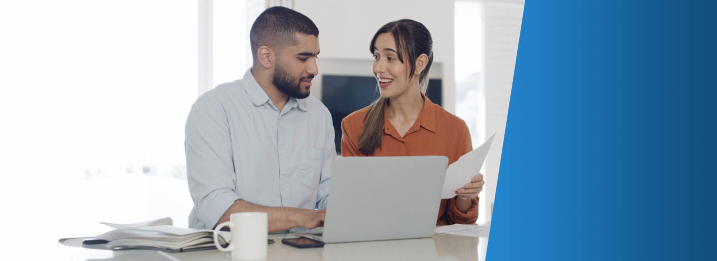 A man and a woman sitting in front of a laptop talking while smiling.