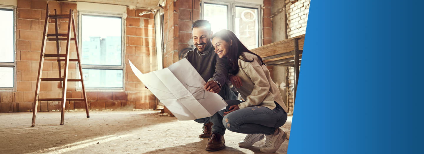 Two people smiling looking at design plans in a room that is being renovated
