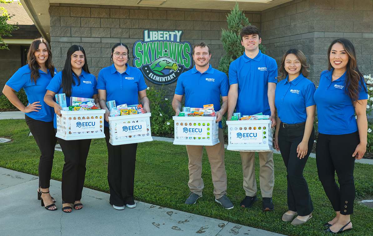 Seven EECU employees wearing matching blue polos, dropping 4 full crates of school supplies to Liberty Elementary