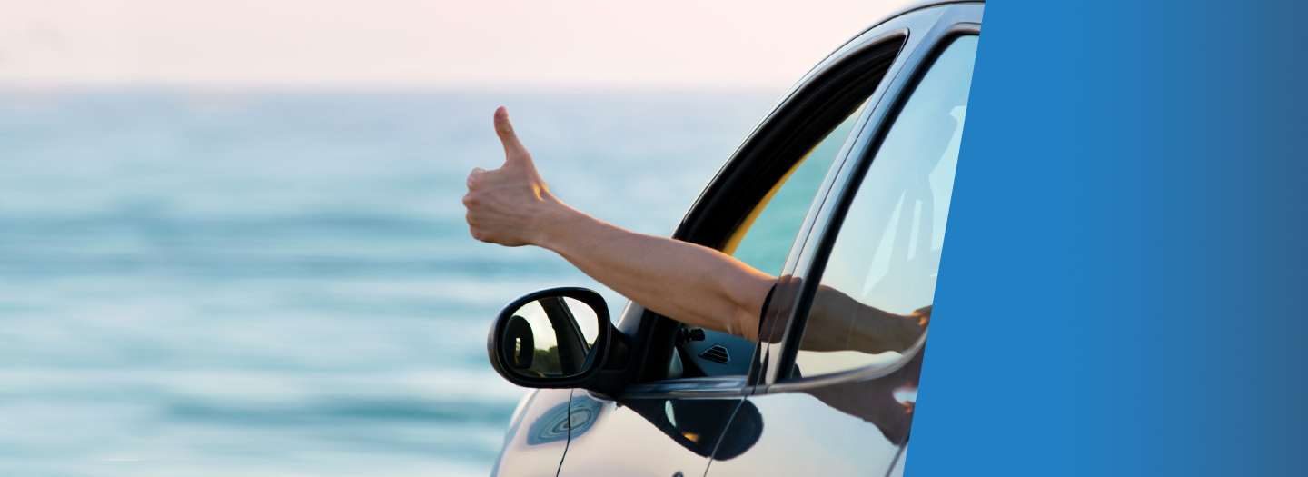 Person with thumbs up out driver window of car overlooking ocean view