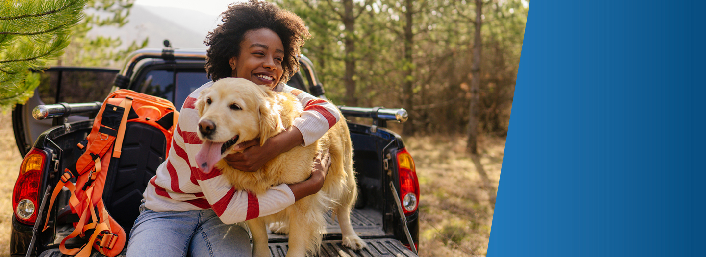 African American woman sitting on the tailgate of her truck in the wilderness hugging her dog