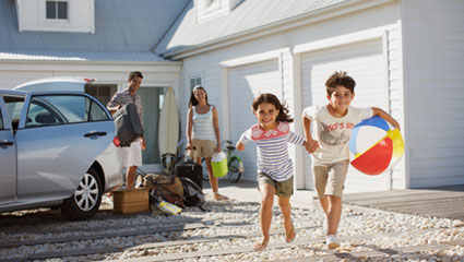 Young couple with kids in front of home packing car