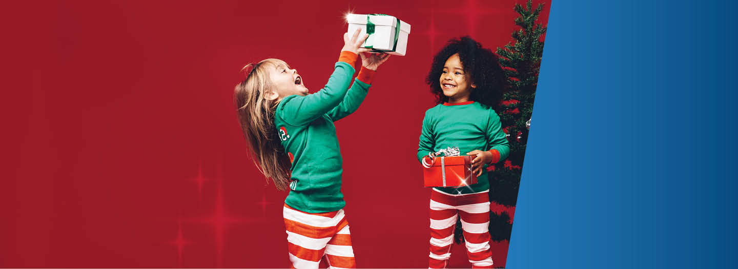 Two excited kids in holiday pajamas with presents