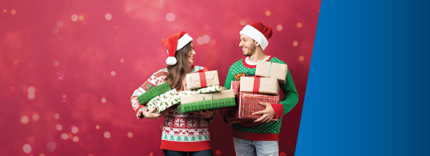 Man And woman wearing Christmas sweaters and Santa hats, holding wrapped presents