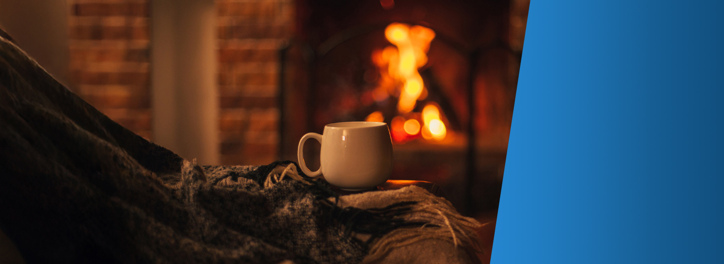 Coffee mug sitting on a stack of blankets in front of a fireplace.